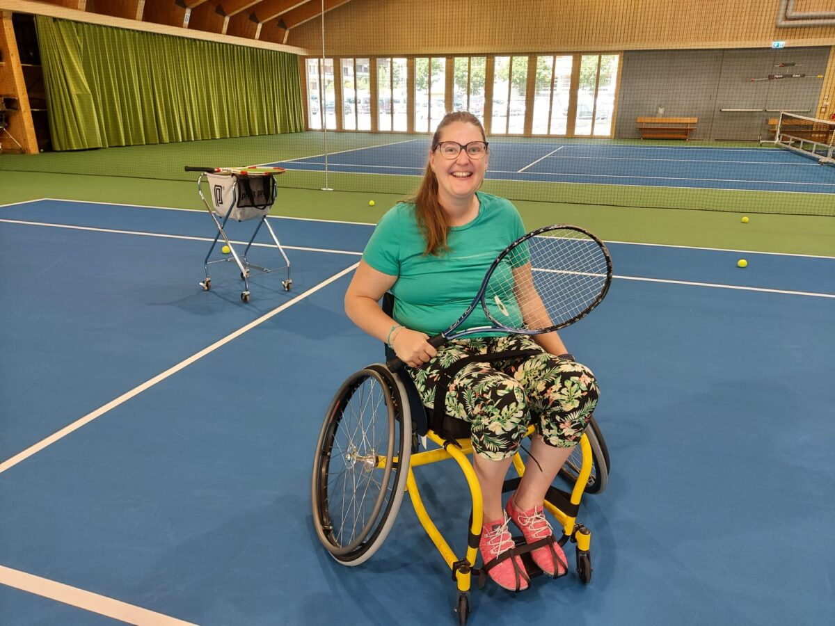 Donna in carrozzina da tennis in una sala interna.