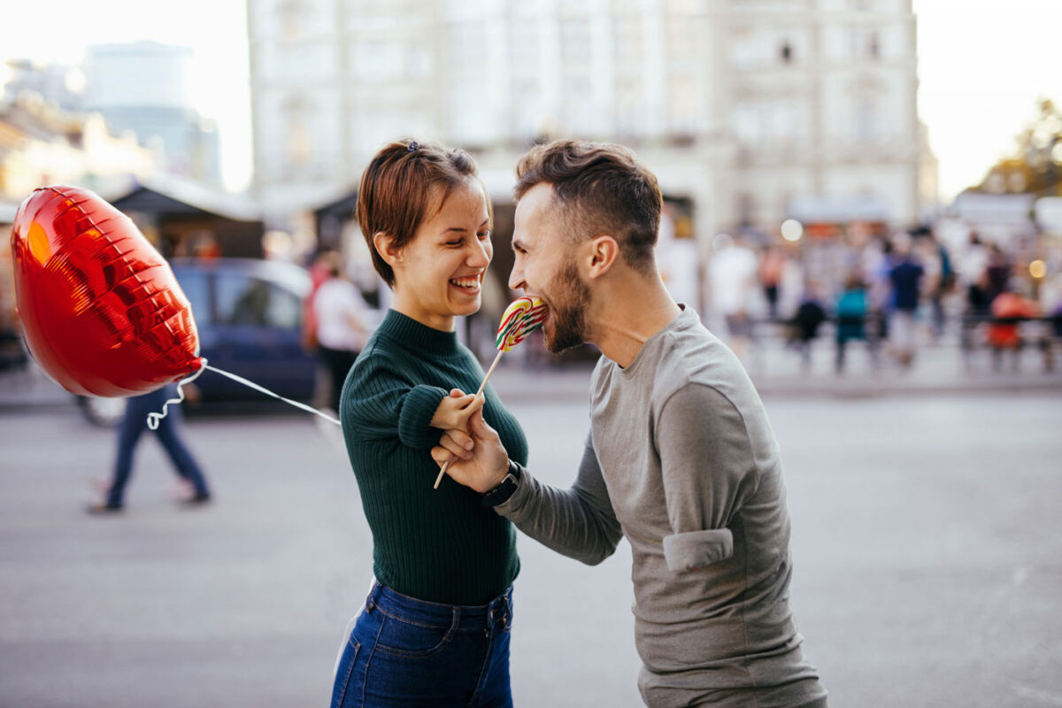 Una coppia che si sorride. Entrambi hanno in mano un lecca-lecca a forma di cuore. La donna ha un braccio accorciato. L'uomo è privo del braccio sinistro.